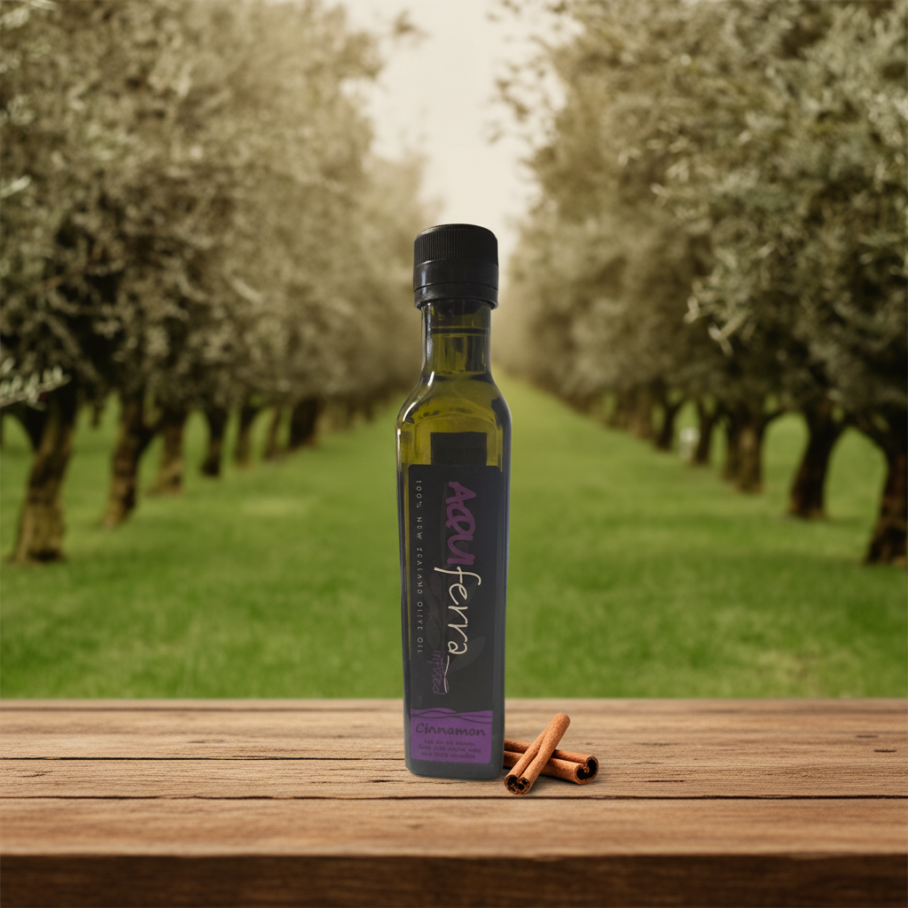Aquiferra Cinnamon olive oil bottle centred on rustic timber with a Hawke’s Bay olive grove softly blurred behind it.