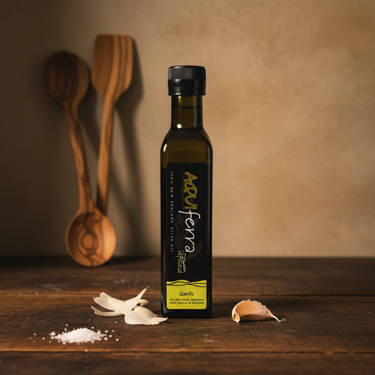 Aquiferra Garlic olive oil bottle on a dark rustic kitchen bench with garlic and subtle Mediterranean props.