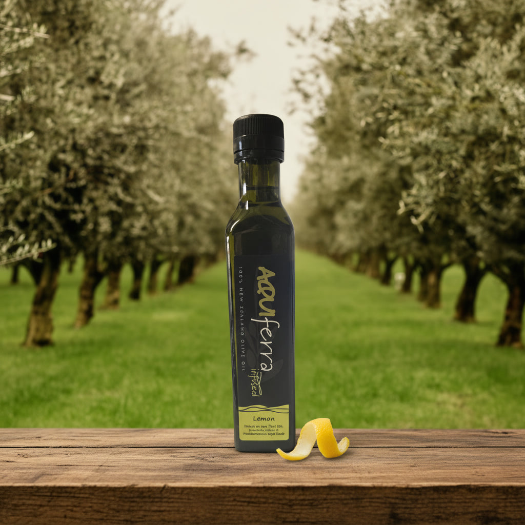 Aquiferra Lemon olive oil bottle centred on rustic timber with a Hawke’s Bay olive grove softly blurred behind it.